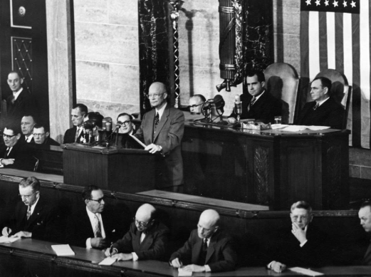 President Eisenhower stands in front of a room of people delivering a speech.